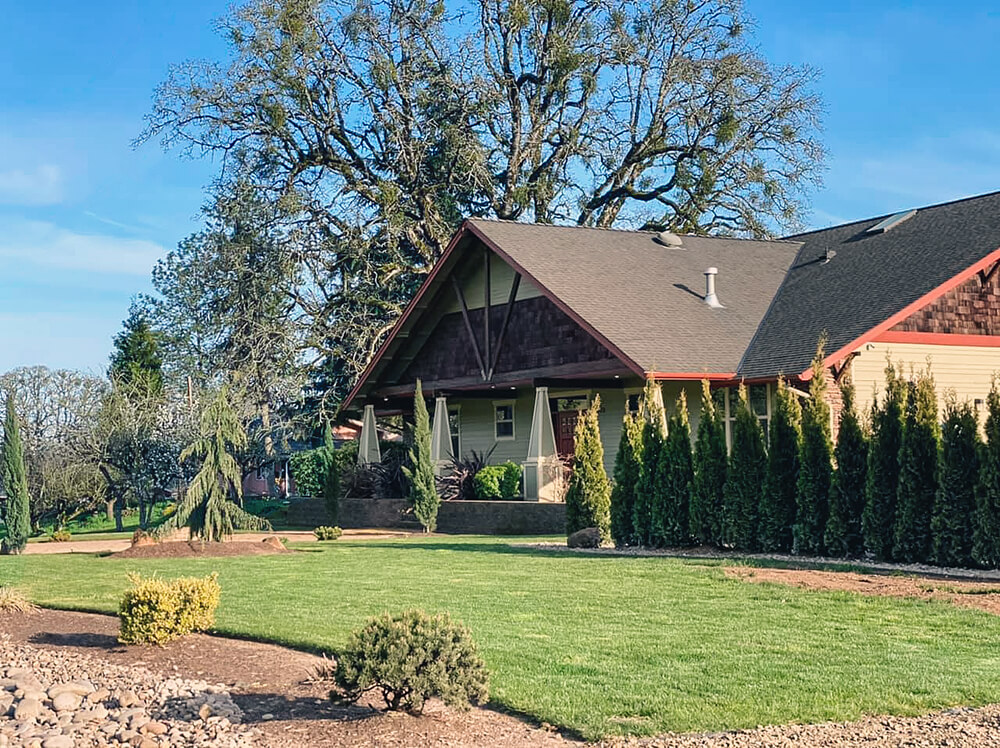 craftsman-style building with grass and large tree in the background