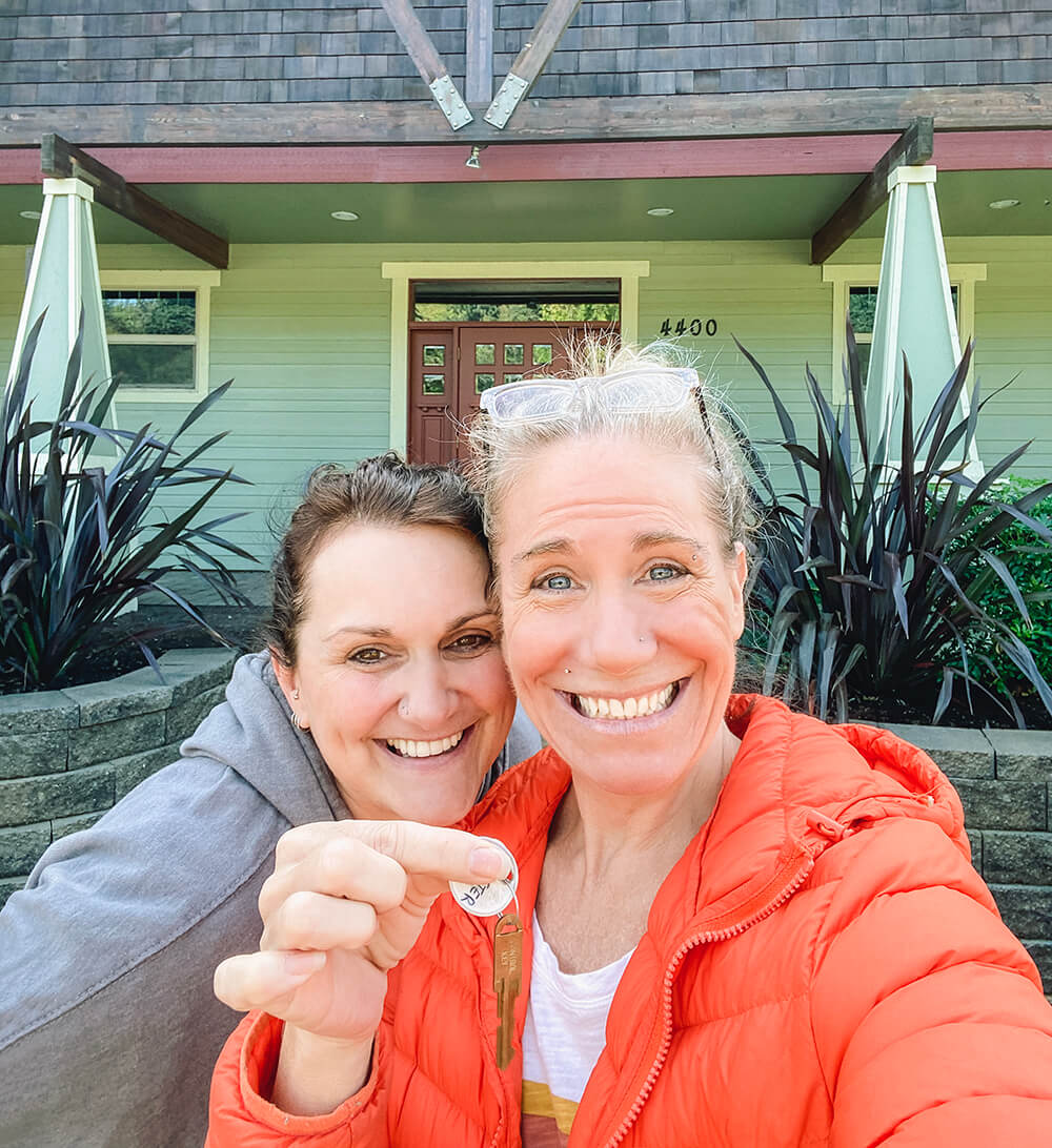 two women in front of building holding up keys